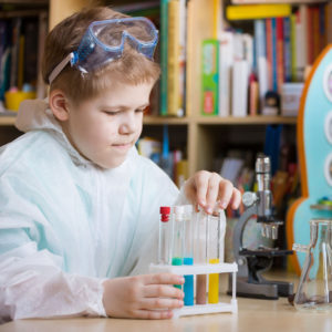 Cute school kid boy sitting at the table making science experiments at home. Learning activities with children at home. Doing water tests. Future profession - scientist.