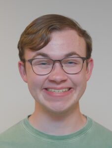A man with glasses on smiling in a green shirt.