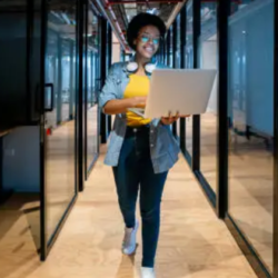 A woman walking in office by having laptop in her hands.