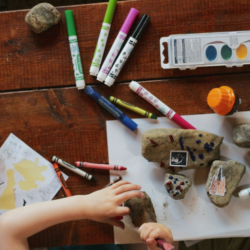 Picture showing colour pens and markers on table along with a baby's hand on table.
