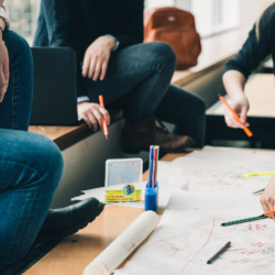 Picture showing group of people sitting in a circle and doing work using pens and charts.